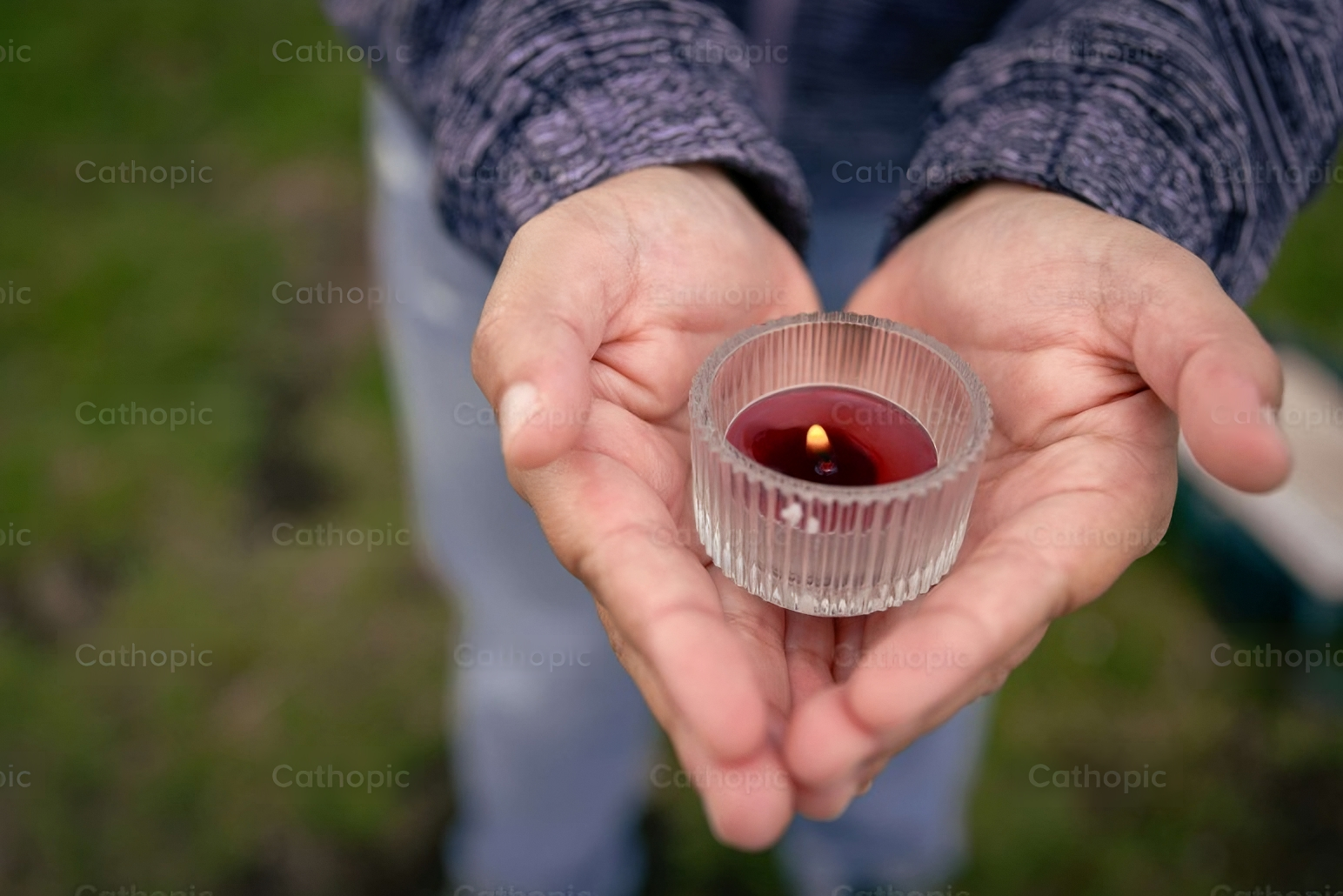 Two hands in the shape of a heart holding candle.