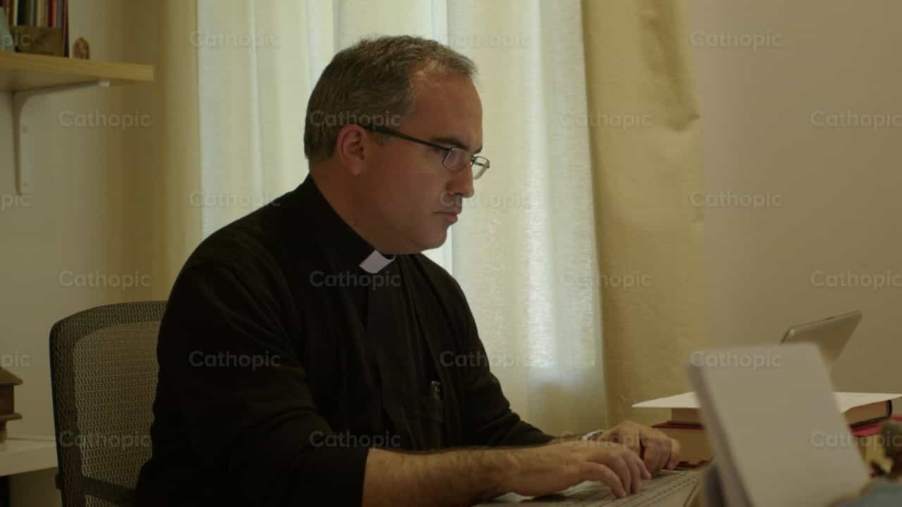 Sacerdote en su oficina frente a la computadora - Banco de vídeos católicos - Fotografía por Almures Studio