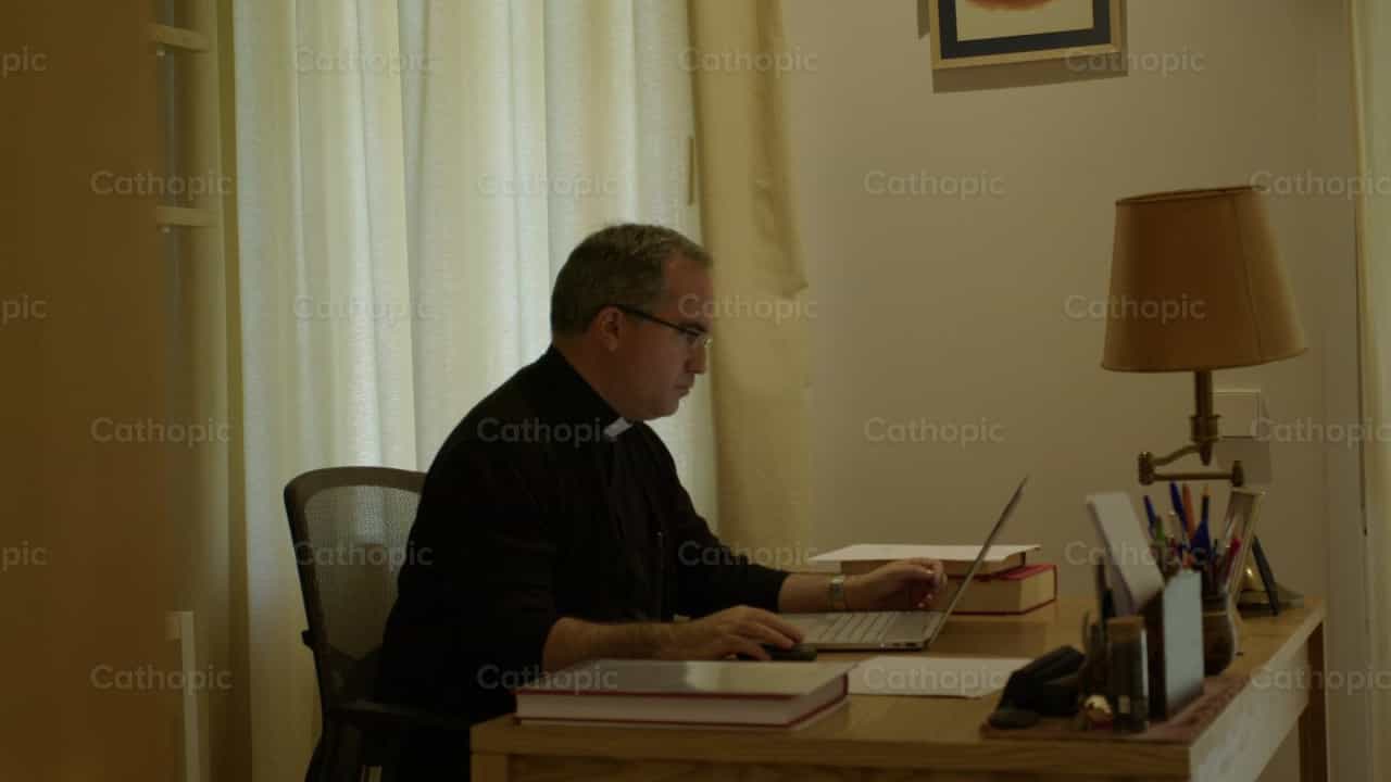 Sacerdote en su oficina frente a la computadora - Banco de vídeos católicos - Fotografía por Almures Studio