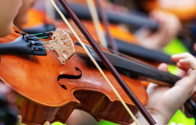 Músico tocando el violín durante un concierto con otros músicos de fondo - Banco de imágenes católicas - Fotografía por Antonio Gravante