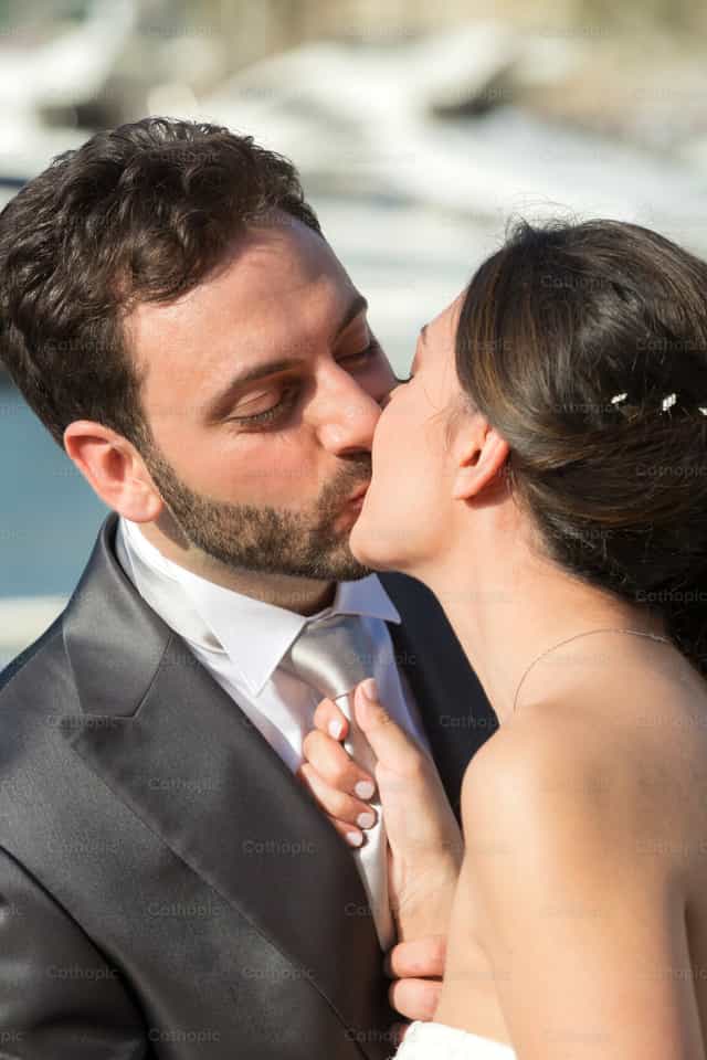 La novia tira de la corbata del novio mientras le besa - Banco de imágenes católicas