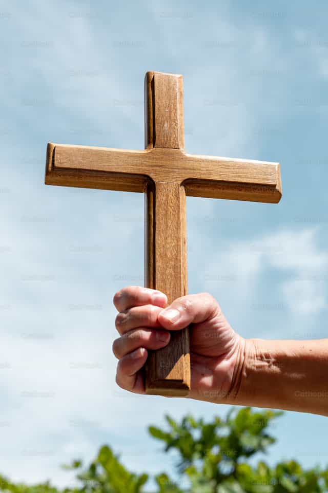 Mano que sostiene una cruz de madera contra un cielo brillante - Banco de imágenes católicas
