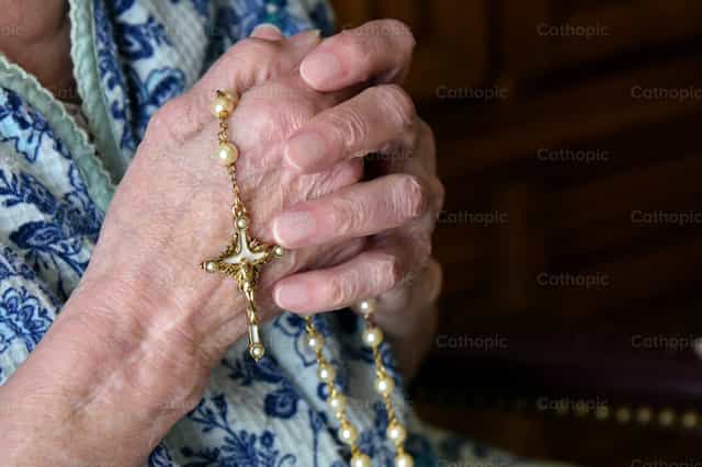 Las manos de una anciana sosteniendo un rosario - Banco de imágenes católicas