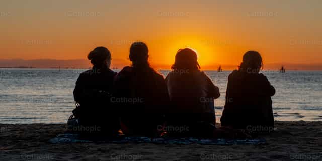 Amigos en la playa viendo el amanecer - Banco de imágenes católicas