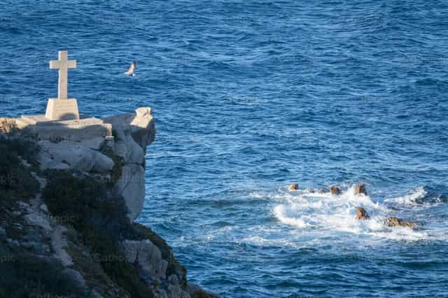 Cruz de piedra sobre el mar, fe y el límite de la naturaleza - Banco de imágenes católicas - Fotografía por Joan Sutter