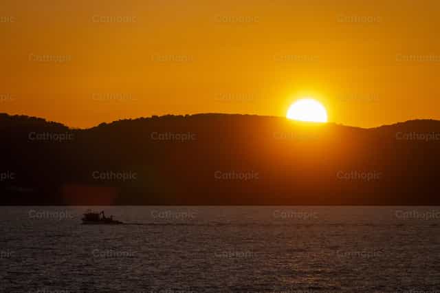 Sunset Over Sea With Silhouetted Boat - Catholic stock images - Photo by Joan Sutter