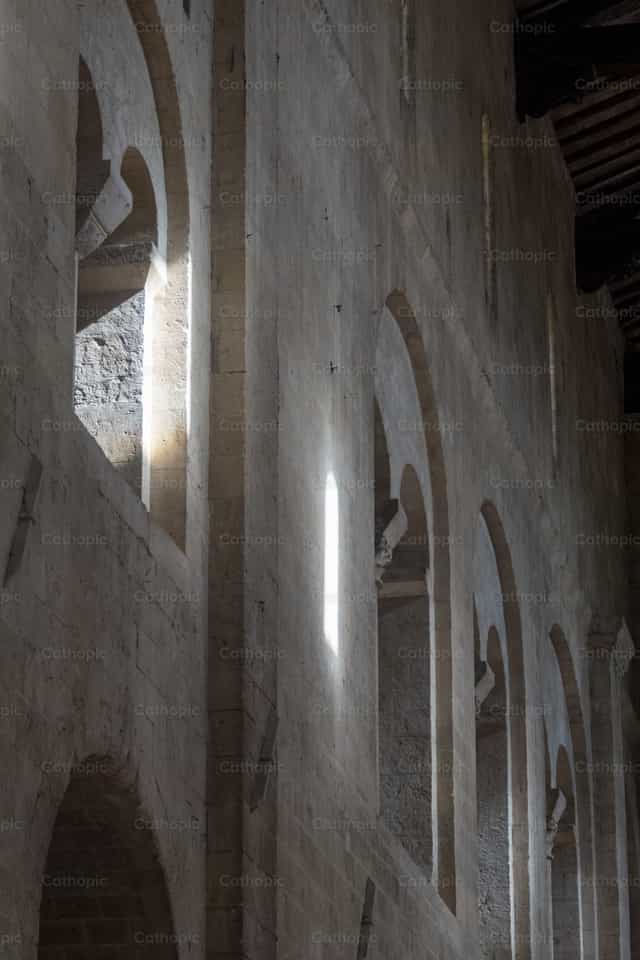 La luz se filtra a través de los arcos románicos. - Banco de imágenes católicas - Fotografía por Joan Sutter