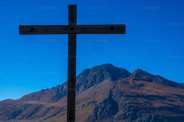 Cruz silueteada contra el pico y el cielo azul - Banco de imágenes católicas - Fotografía por Joan Sutter
