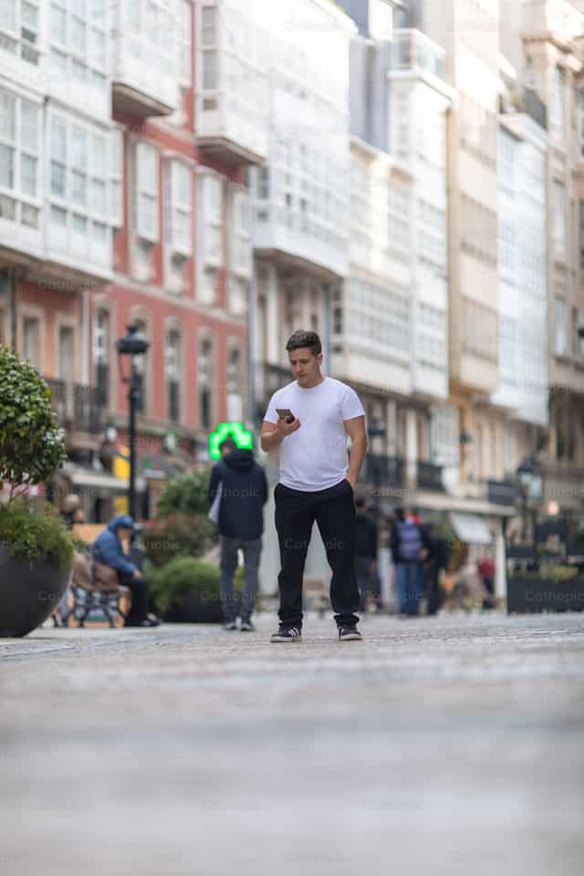 Joven mirando el teléfono móvil en la calle - Banco de imágenes católicas - Fotografía por Yandry Fernández Perdomo
