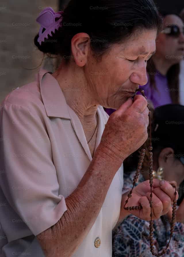 Mujer besando un rosario - Banco de imágenes católicas - Fotografía por Carolina BR