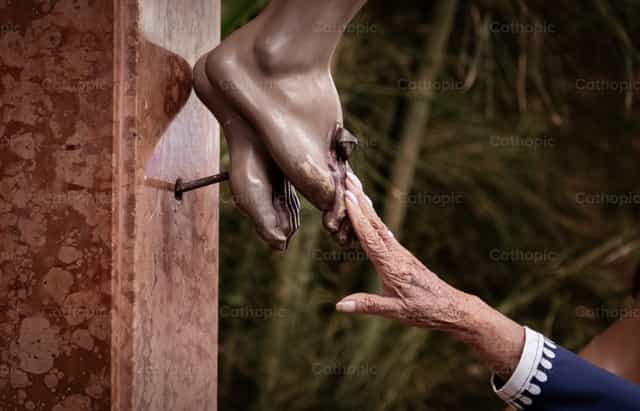 Mano tocando el pie de Cristo - Banco de imágenes católicas - Fotografía por Carolina BR