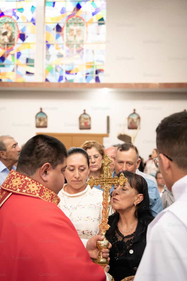 Mujer besa cruz dorada en acto litúrgico - Banco de imágenes católicas - Fotografía por Carolina BR