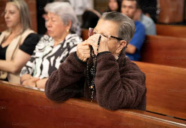 Mujer rezando con rosario en iglesia - Banco de imágenes católicas - Fotografía por Carolina BR