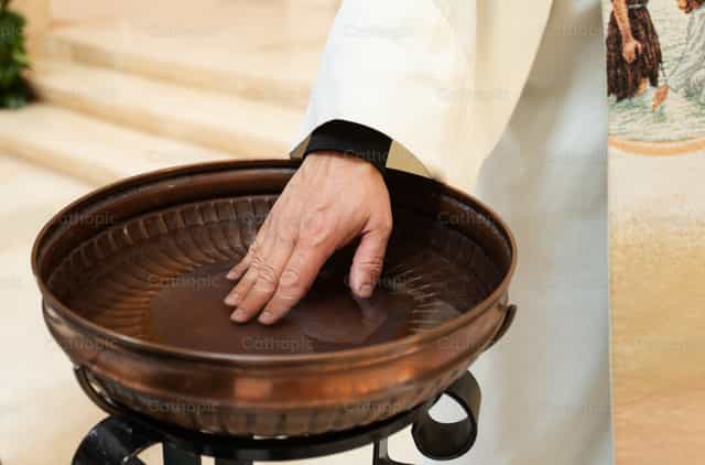 La mano del sacerdote tocando el agua en la pila bautismal - Banco de imágenes católicas