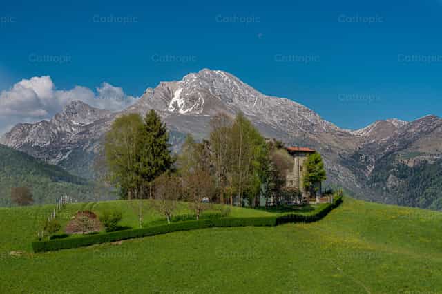 Casa de campo de piedra entre los verdes prados y las cumbres de las montañas Orobie de Bérgamo - Banco de imágenes católicas - Fotografía por Pierluigi Palazzi