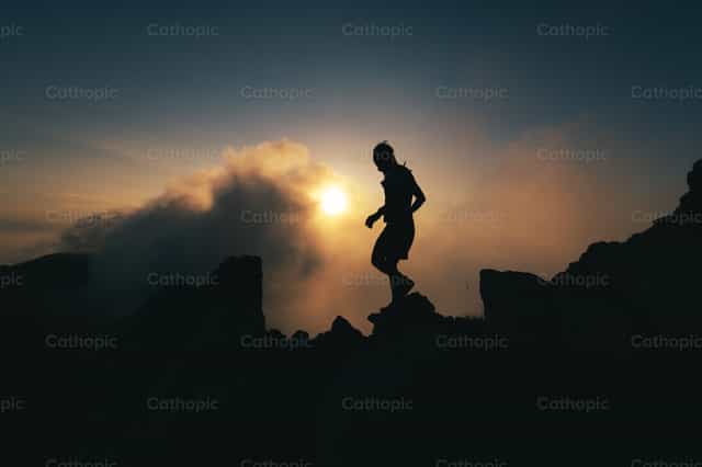 Un hombre en silueta camina por una cresta rocosa durante una meditación solitaria - Banco de imágenes católicas - Fotografía por Michelangelo Oprandi