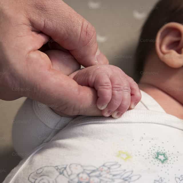Padre sosteniendo la mano de su bebé recién nacido - Banco de imágenes católicas
