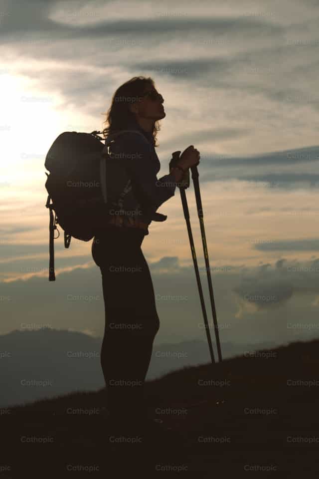 Una chica solitaria con su mochila descansa y observa el panorama - Banco de imágenes católicas - Fotografía por Michelangelo Oprandi