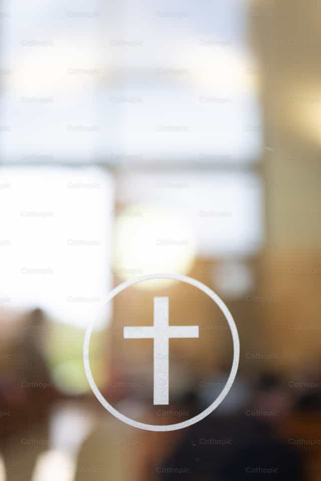 Cruz en puerta de vidrio con fondo suave del interior de la iglesia - Banco de imágenes católicas - Fotografía por Cori Nations