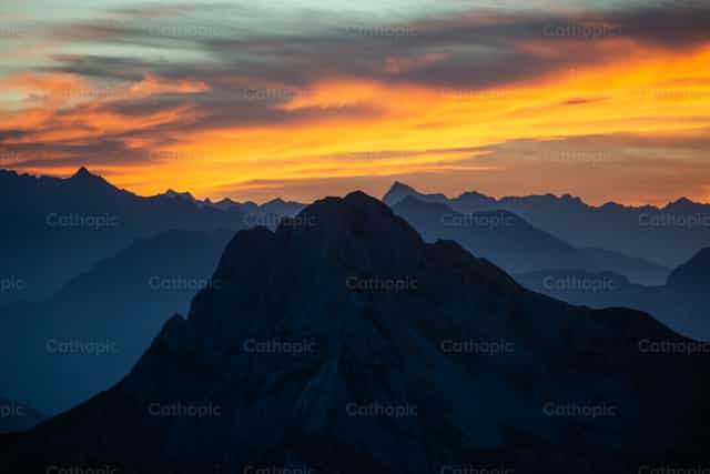 Cruz en la cima al atardecer, en medio de la majestad de la Creación. - Banco de imágenes católicas
