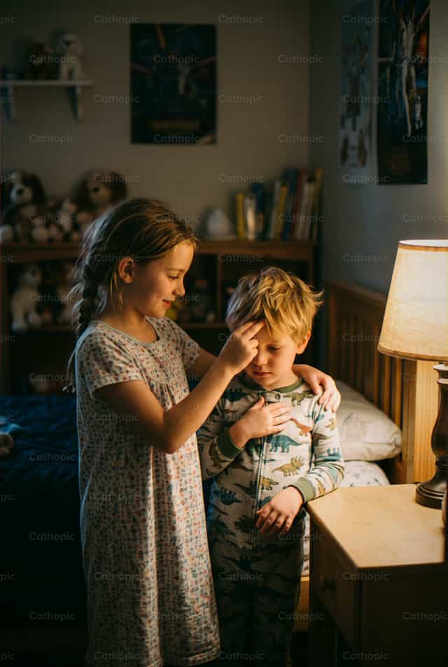 Una bambina che fa il segno della croce sul suo fratellino - Immagini stock cattoliche - Foto di Enma Bastidas