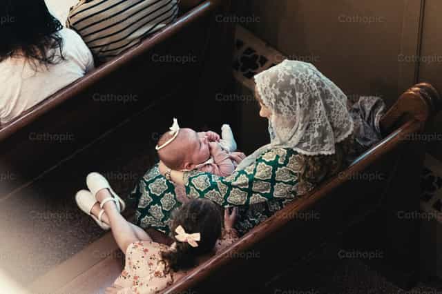 Una madre sostiene a su bebé durante la misa - Banco de imágenes católicas - Fotografía por Carlos Sierra