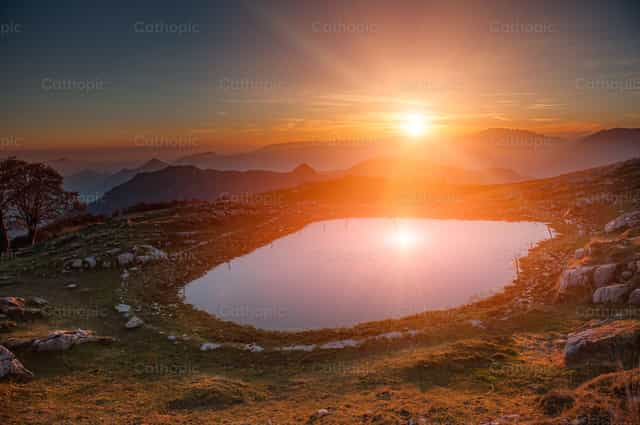 Lago de montaña donde se refleja el sol al atardecer. - Banco de imágenes católicas - Fotografía por Pierluigi Palazzi