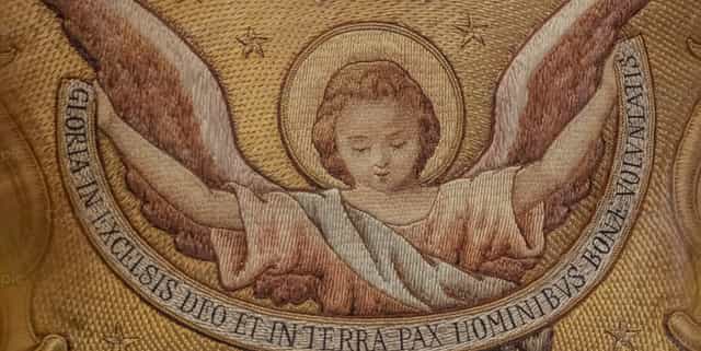Bordado dorado de un ángel con texto en latín - Banco de imágenes católicas - Fotografía por Joan Sutter