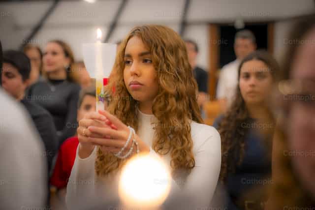 Joven mujer sosteniendo una vela en una celebración - Banco de imágenes católicas - Fotografía por Thiago Damião P. Silva