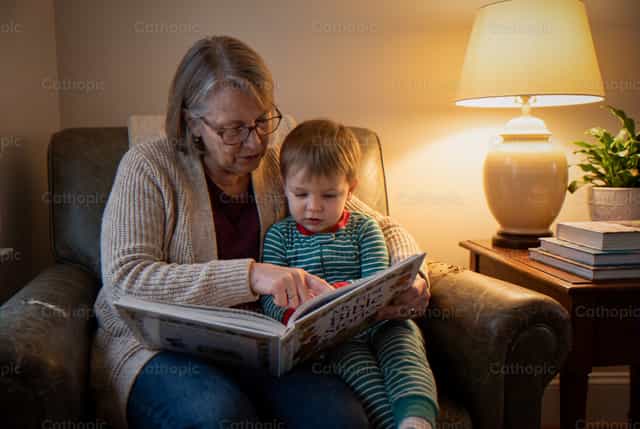 Une femme âgée lit une Bible illustrée à un jeune enfant - Images catholiques de stock - Photo de Noemí Márquez