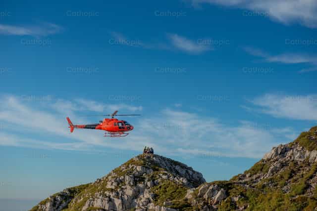 Helicóptero rojo volando sobre picos de montaña - Banco de imágenes católicas - Fotografía por Pierluigi Palazzi