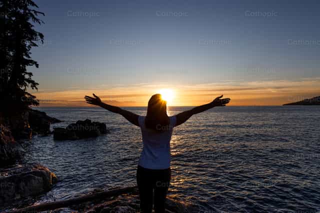 Mujer abrazando el sol poniente - Banco de imágenes católicas - Fotografía por Paul Van Buekenhout