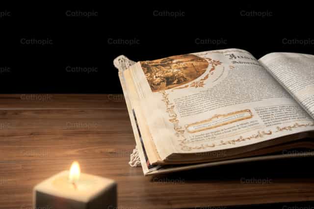 Biblia y vela sobre mesa de madera con fondo negro - Banco de imágenes católicas - Fotografía por Piero Insfran