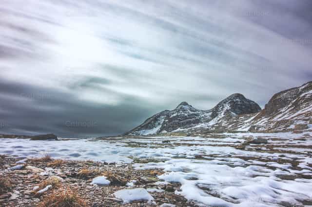 Paisaje rocoso cubierto de nieve con cielo nublado y picos montañosos - Banco de imágenes católicas
