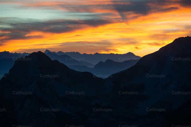 Cruz en la cima al atardecer, en medio de la majestad de la Creación. - Banco de imágenes católicas