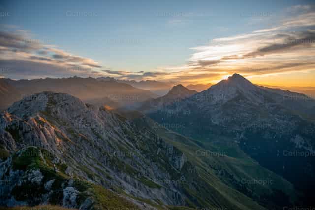 Cruz en la cima al atardecer, en medio de la majestad de la Creación. - Banco de imágenes católicas