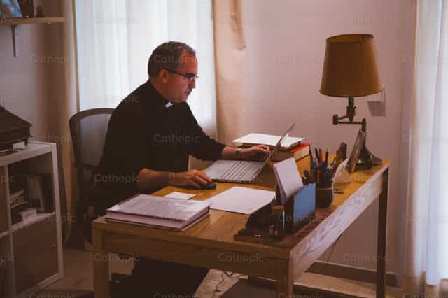 Sacerdote trabajando en su oficina - Banco de imágenes católicas - Fotografía por Almures Studio
