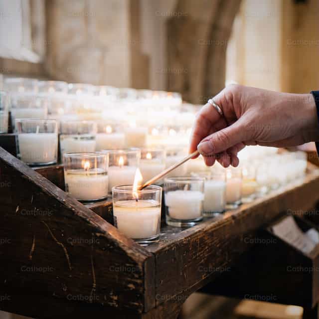 Hand zündet Votivkerzen in der Kirche während des Gebets an - Katholische Stockfotos