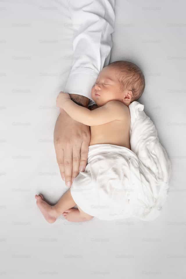 Un bebé recién nacido sostenido de la mano de su padre - Banco de imágenes católicas - Fotografía por Clina CG