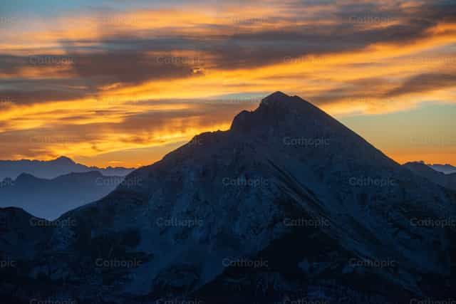 Cruz en la cima al atardecer, en medio de la majestad de la Creación. - Banco de imágenes católicas