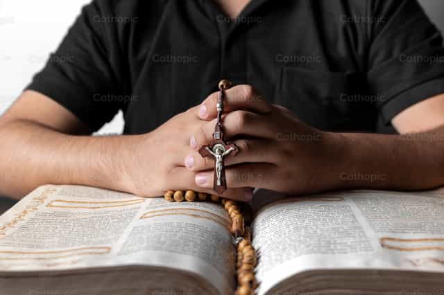 A boy praying the rosary over a bible - Catholic stock images - Photo by Piero Insfran