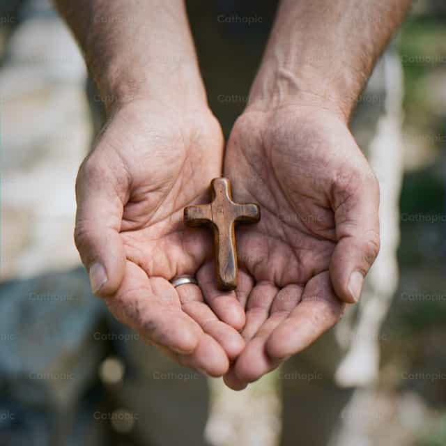 Mãos masculinas segurando uma cruz de madeira ao ar livre com luz natural - Imagens católicas de stock
